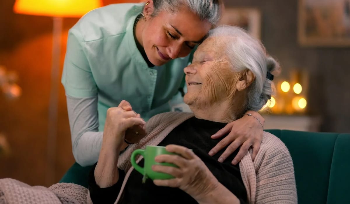 Caregiver warmly assisting an elderly woman at home